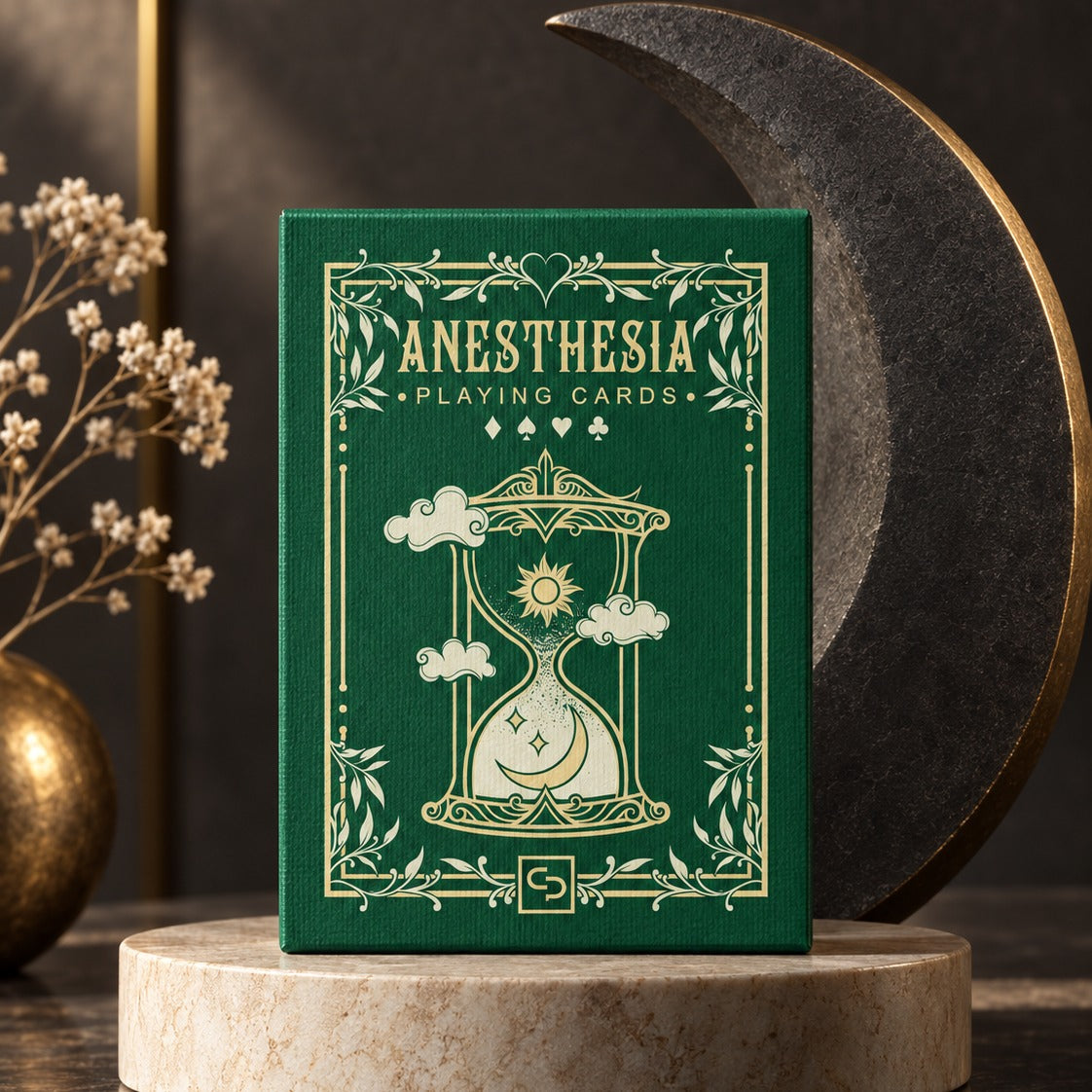 The Anesthesia Playing Cards tuck box, gold-foiled on green, raised on a stone plinth